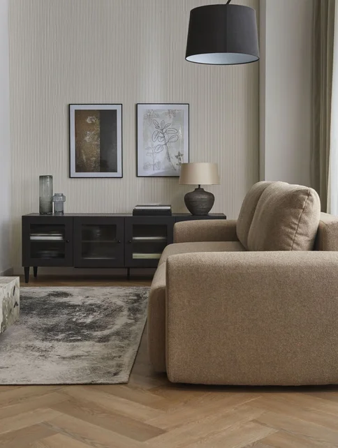 Beżowa sofa na tle lameli i czarnej komody z obrazami